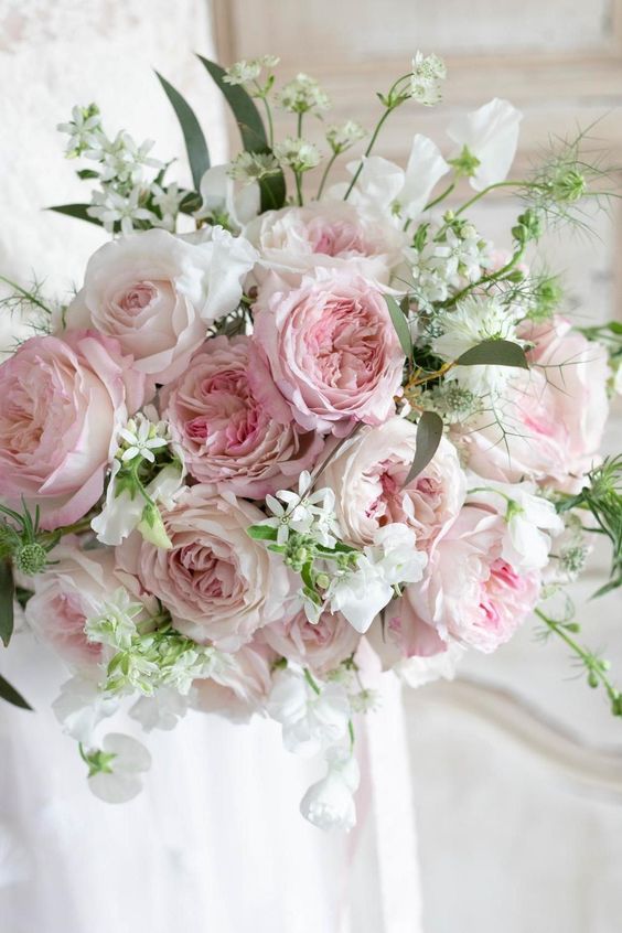 a light pink and white wedding bouquet with greenery and white fillers is a delicate and subtle touch of color to the bridal look