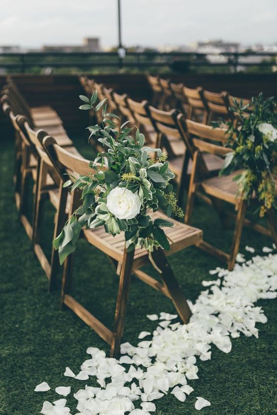 a lovely and fresh spring wedding aisle with white petals on the ground, with white ranunculus and greenery on the chairs