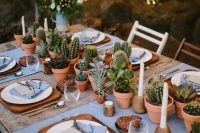 a lovely backyard wedding tablescape with blue linens, wooden placemats, potted succulents and cacti plus candles