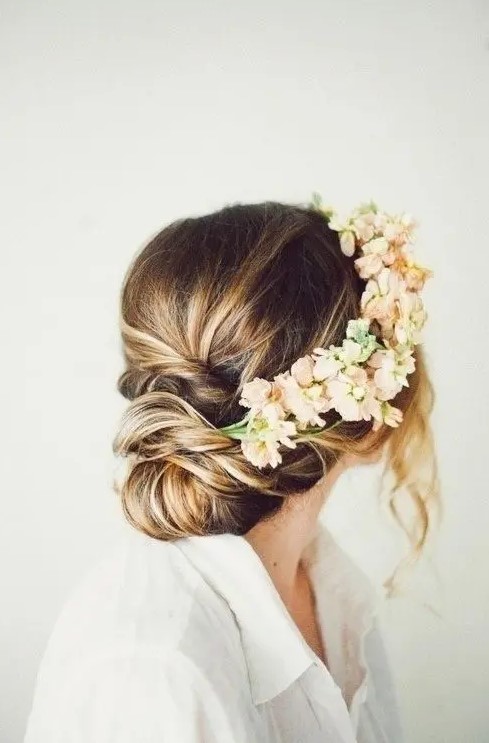 a low updo with a twisted low bun and neutral and blush blooms and some locks down to frame the face is a beautiful idea for a boho bride