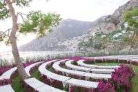 a modern and super bold wedding aisle with white semi circle benches and bright purple blooms lining them