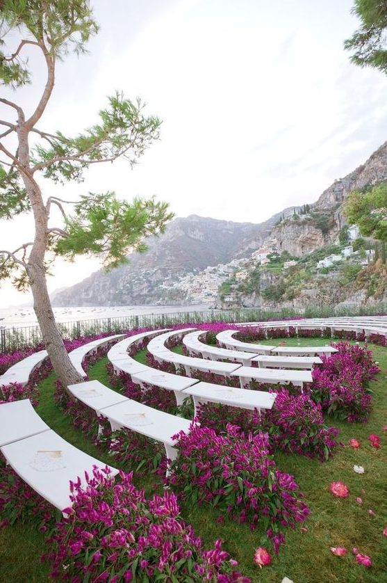 a modern and super bold wedding aisle with white semi circle benches and bright purple blooms lining them