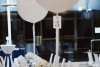 a modern glam wedding table with a navy table runner, white napkins, white floral centerpieces and white candles plus balloons