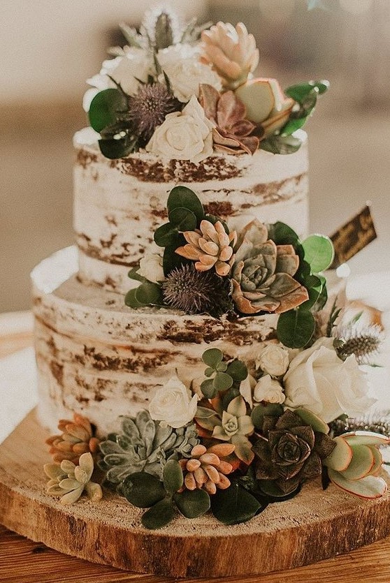 a naked wedding cake with greenery, succulents, thistles and white blooms for a rustic wedding