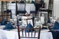 a nautical wedding table setting with a navy table runner and napkins, pebbles and candle lanterns is very chic