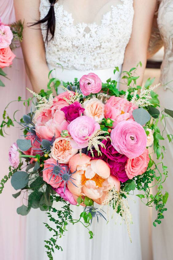 a pink wedding bouquet with bright, coral and peachy pink blooms, greenery, thistles and berries is a bold and catchy idea for a summer wedding