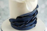 a plain white wedding cake with navy ruffles, a large white sugar bloom on top is very chic