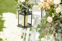 a pretty and chic spring wedding aisle with neutral petals on the ground, with candle lanterns decorated with greenery and white blooms