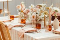a pretty and cozy backyard wedding tablescape with a pastel and neutral floral centerpiece, with striped linens, blush candles and amber glasses