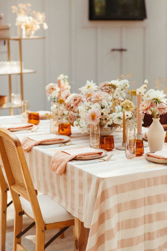 a pretty and cozy backyard wedding tablescape with a pastel and neutral floral centerpiece, with striped linens, blush candles and amber glasses