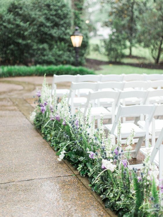 a pretty fresh spring wedding aisle with greenery and fern, white and purple blooms plus thistles is amazing
