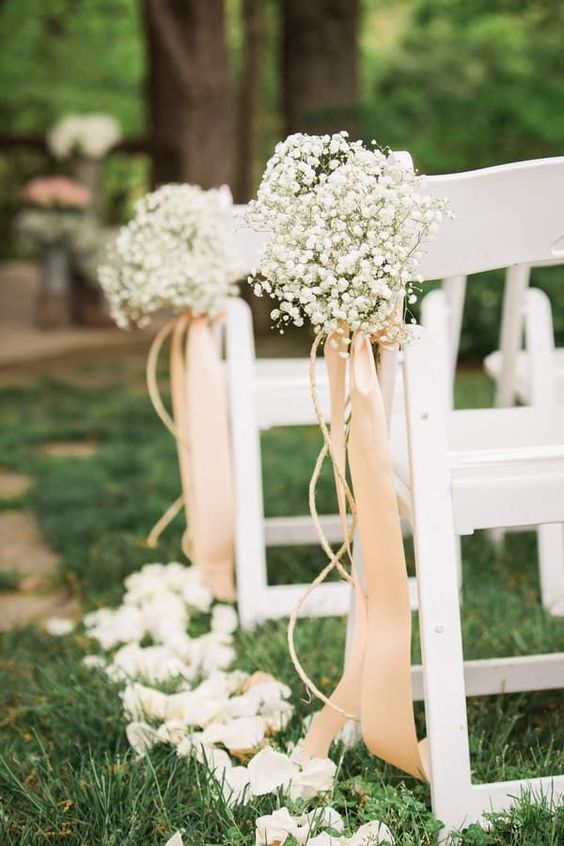a refined vintage wedding aisle with white baby's breath arrangements with blush ribbons and white petals on the ground is chic
