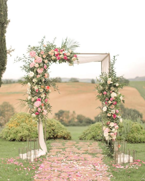 a refined wedding arch made of branches, neutral fabric, pink and hot pink blooms and greenery plus candle lanterns