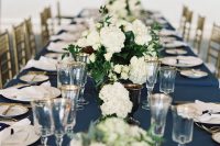 a refined wedding table setting with a navy tablecloth, white napkins, white hydrangeas and touches of gold