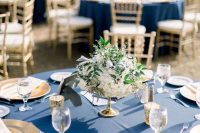 a refined wedding tablescape with a navy tablecloth, gold chargers and candle lanterns and a white floral centerpiece