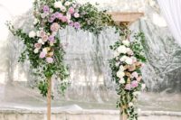 a refreshing spring wedding arch done with greenery and neutral and lilac blooms and candle lanterns