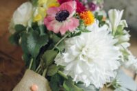 a relaxed and bright wedding bouquet with a burlap wrap and coral buttons is a cool idea for a rustic wedding