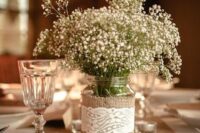 a rustic wedding centerpiece of a jar wrapped with burlap and lace, with baby’s breath is a lovely idea for a rustic wedding