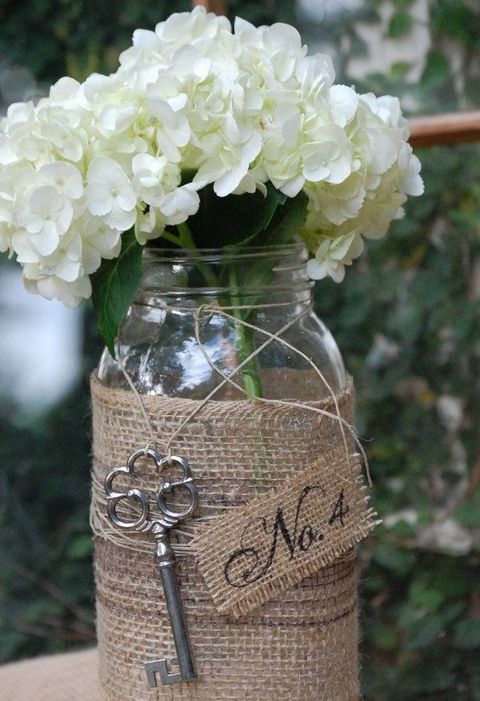 a rustic wedding centerpiece of a jar wrapped with burlap, twine and with a vintage key, white hydrangeas for a rustic wedding
