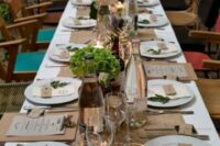 a rustic wedding tablescape with a burlap runner, pillar candles, white blooms and greenery and kraft paper seating cards