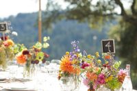 a simple and bold wedding tablescape with bold florals and greenery, candles and bottles with table numbers plus neutral linens