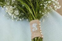 a simple white wedding bouquet with baby’s breath and roses, a wrap of burlap with an embroidered monogram and pearl buttons