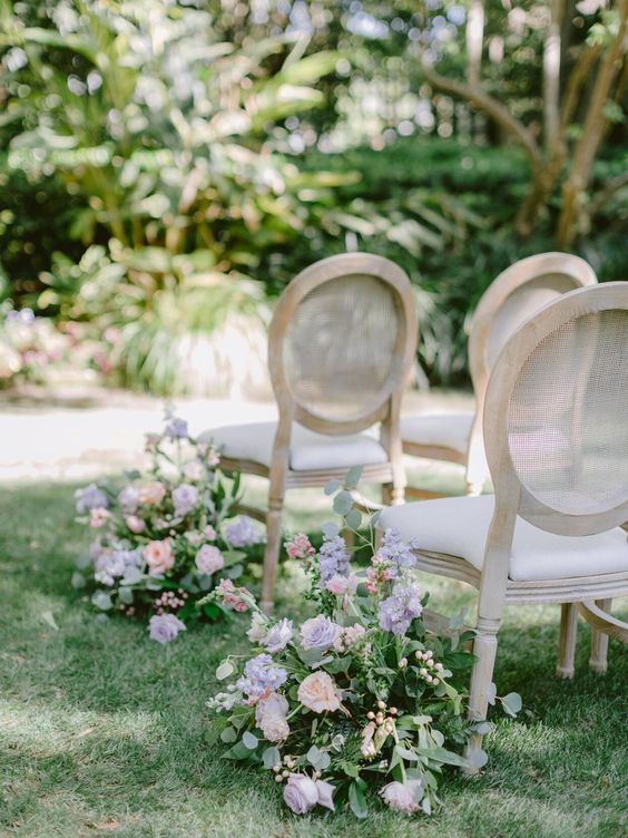 a sophisticated spring garden wedding aisle with blush and lilac blooms, berries and greenery plus chic vintage chairs