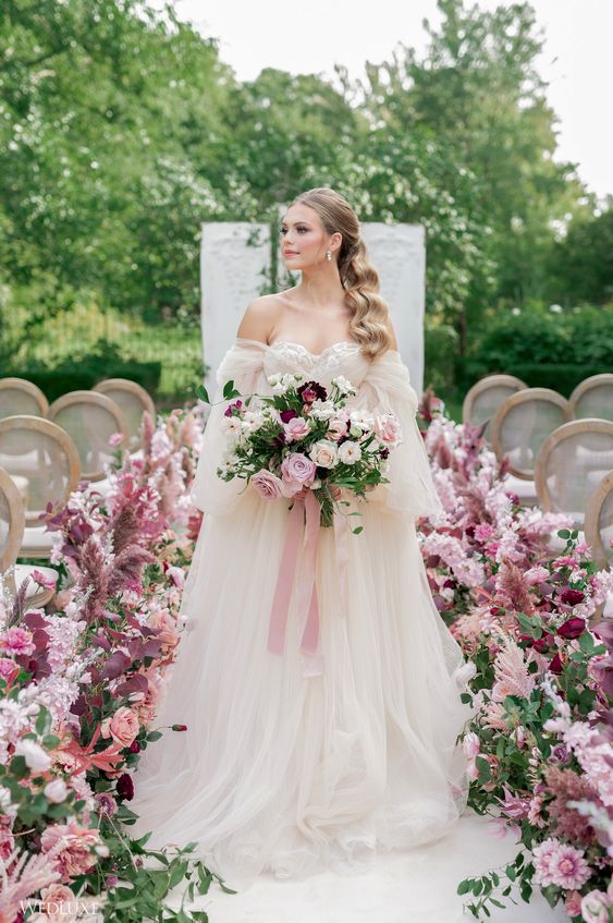 a sophisticated spring wedding aisle decorated with pink, lilac, mauve blooms and greenery creates a fairy-tale feel here