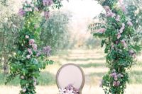 a spring wedding arch covered with greenery and spruced up with lilac and purple blooms is gorgeous
