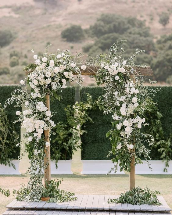 a spring wedding arch with greenery and lush white blooms is a chic idea for a modern or rustic ceremony outdoors