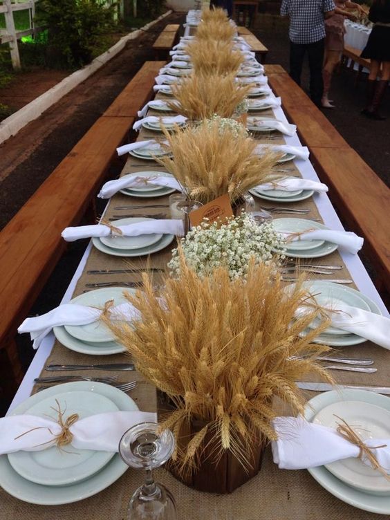 a stylish rustic wedding tablescape with wheat arrangements and baby's breath ones, a burlap tablecloth and green plates