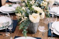 a stylish wedding tablescape with navy napkins, white porcelain, chic white floral and greenery centerpieces and silver