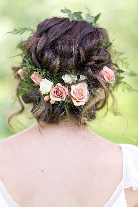 A wavy low updo with a twisted top and some waves down, with greenery, pink and white roses feels very summer like