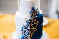 a white and navy watercolor wedding cake with gold geometric detailing for a chic look