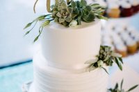 a white buttercream wedding cake decorated with succulents and greenery, with a calligraphy gold glitter topper for a slight glam touch