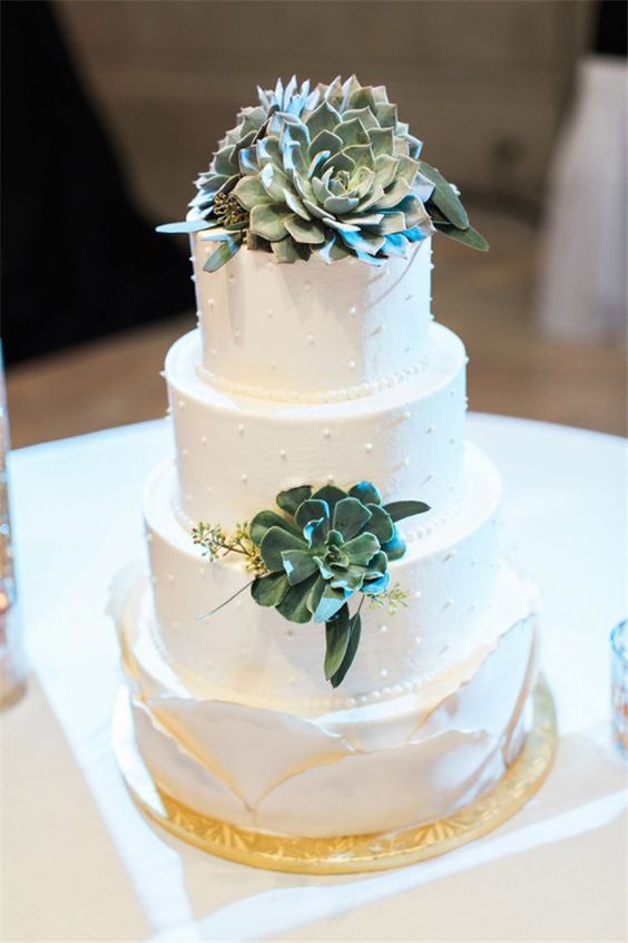 a white buttercream wedding cake with pearls, succulents and greenery and a scallop tier as the lower one is a lovely idea for a refined wedding