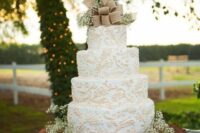 a white wedding cake with beautiful patterns, baby’s breath and a large burlap bow on top for a rustic wedding