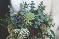 a winter wedding bouquet composed of greenery, succulents, berries and small white blooms plus long ribbons