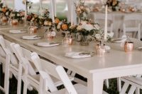 an elegant and chic backyard wedding tablescape with copper mugs, elegant tall candles, neutral and orange blooms and neutral linens