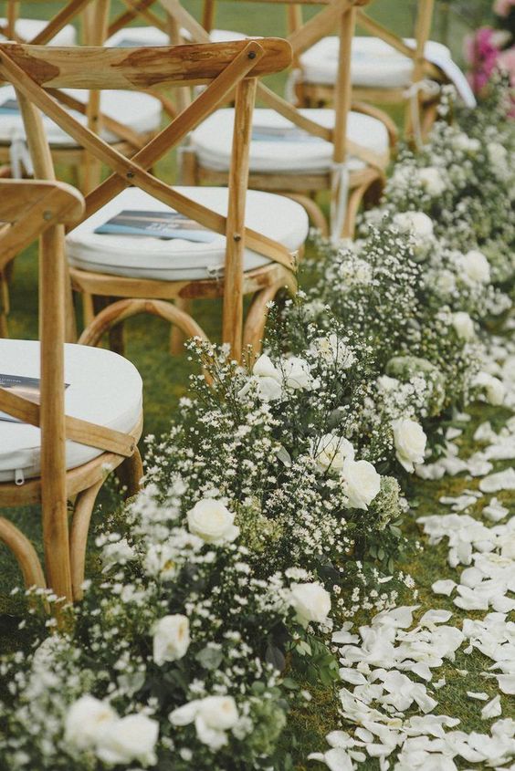 an elegant spring wedding aisle with white petals on the ground and greenery and white blooms lining up the aisle is chic