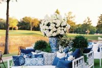 an elegant white and navy wedding lounge with stylish furniture, lots of printed pillows and white floral arrangements