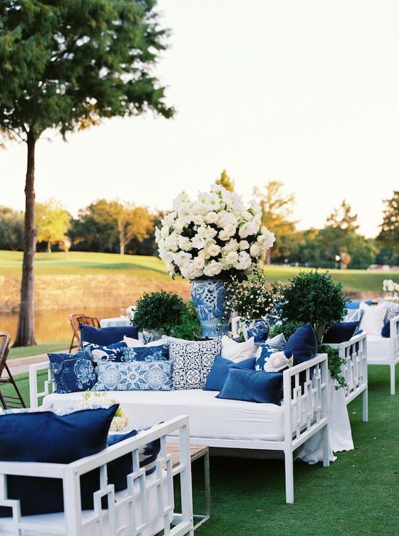 an elegant white and navy wedding lounge with stylish furniture, lots of printed pillows and white floral arrangements