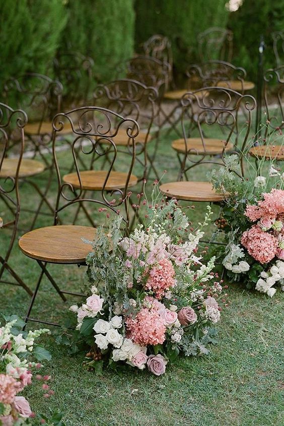 an exquisite spring wedding aisle with a vintage feel, done with greenery, pink, mauve and white blooms and vintage chairs