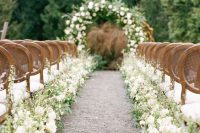 an exquisite spring wedding aisle with white blooms and greenery lining up the aisle and vintage chairs is gorgeous