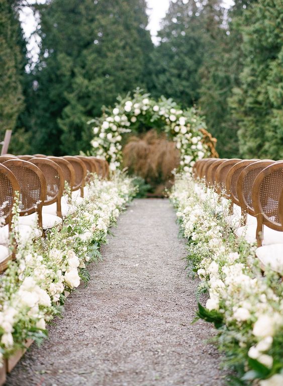 an exquisite spring wedding aisle with white blooms and greenery lining up the aisle and vintage chairs is gorgeous