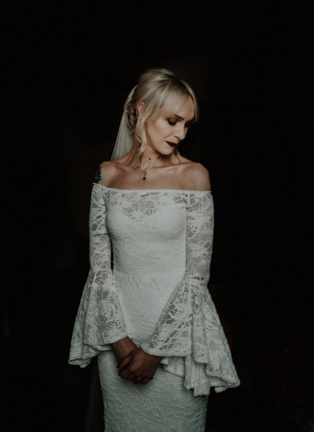 an off the shoulder lace sheath wedding dress with bell sleeves and a dark lipstick for a moody gothic wedding