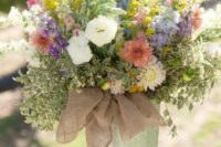 an oversized rustic wedding centerpiece of a bucket with a burlap bow, bright and neutral blooms and greenery is amazing