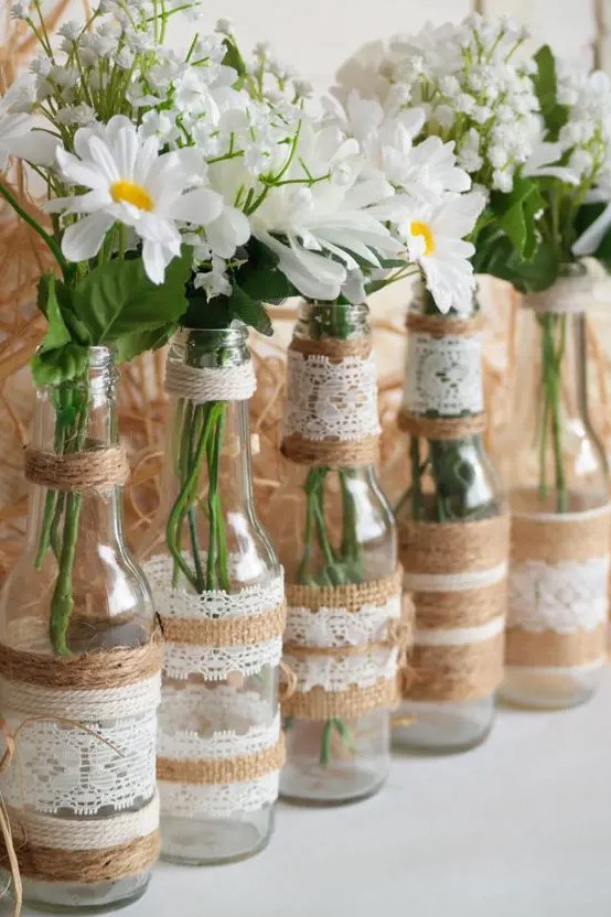 bottles wrapped with lace and twine, with baby's breath and daisies are simple DIY wedding centerpiece you can make fast