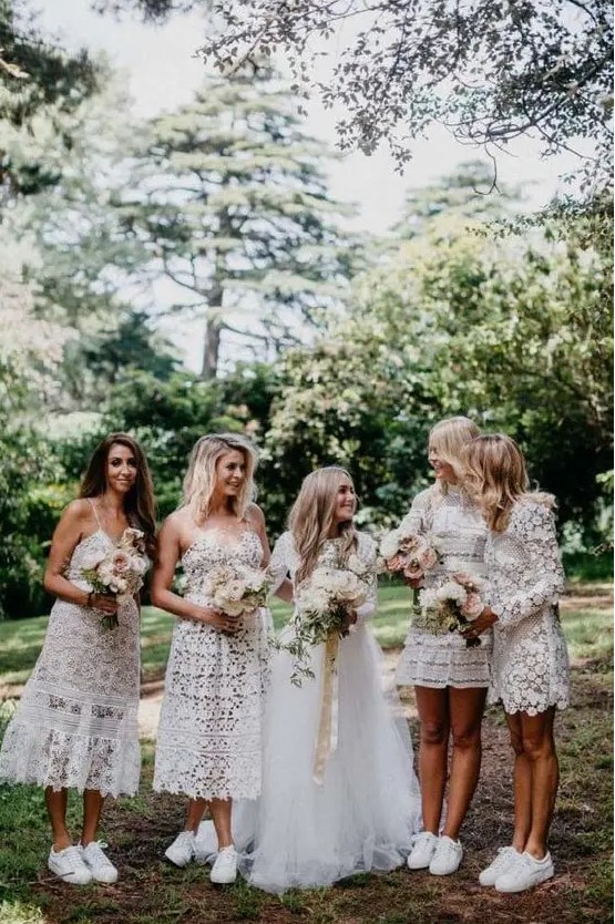 mismatching white boho lace mini and midi bridesmaid dresses and white sneakers for maximal comfort at the wedding