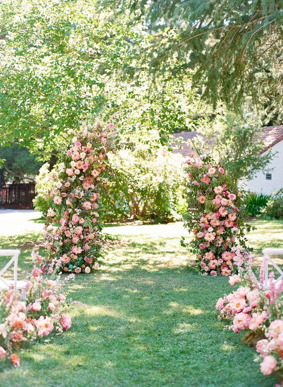 a beautiful wedding ceremony space done with an altar with lush greenery and pink blooms, with matching blooms lining up the aisle